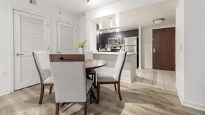 Un coin repas avec une table ronde et quatre chaises, une cuisine équipée d’appareils électroménagers modernes et une porte en bois.