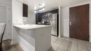 Une cuisine moderne dotée d’un îlot central, d’appareils électroménagers en acier inoxydable et d’une porte en bois foncé.