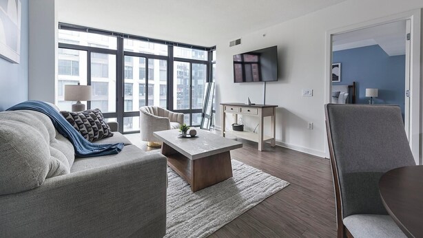Ein modernes Wohnzimmer mit Sofa, Sessel, Couchtisch und Fernseher an der Wand.