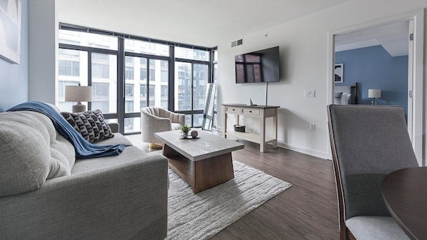 Ein modernes Wohnzimmer mit Sofa, Sessel, Couchtisch und Fernseher an der Wand.