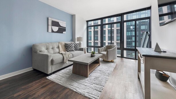 Ein modernes Wohnzimmer mit Sofa, Couchtisch und Sessel, großen Fenstern mit Blick auf die Stadt und einer minimalistischen Einrichtung.