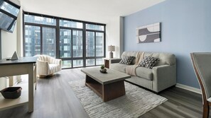 Ein modernes Wohnzimmer mit einer Couch, einem Couchtisch und Blick auf Gebäude durch große Fenster.