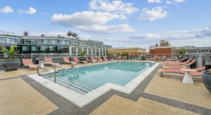 A rooftop pool with lounge chairs, a modern building with glass windows, and a brick structure in the background. - Landing | Stunning 2BD, Courtyard (Washington)