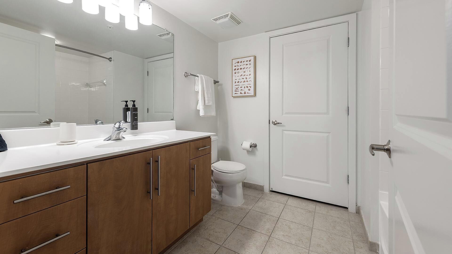 A modern bathroom with a large mirror, a sink, a toilet, and a shower area.