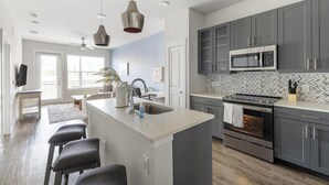 A modern kitchen with grey cabinets, a stainless steel oven, and a herringbone tile backsplash. - Landing | Chic 1BD, Gym, Clubhouse (Dallas)