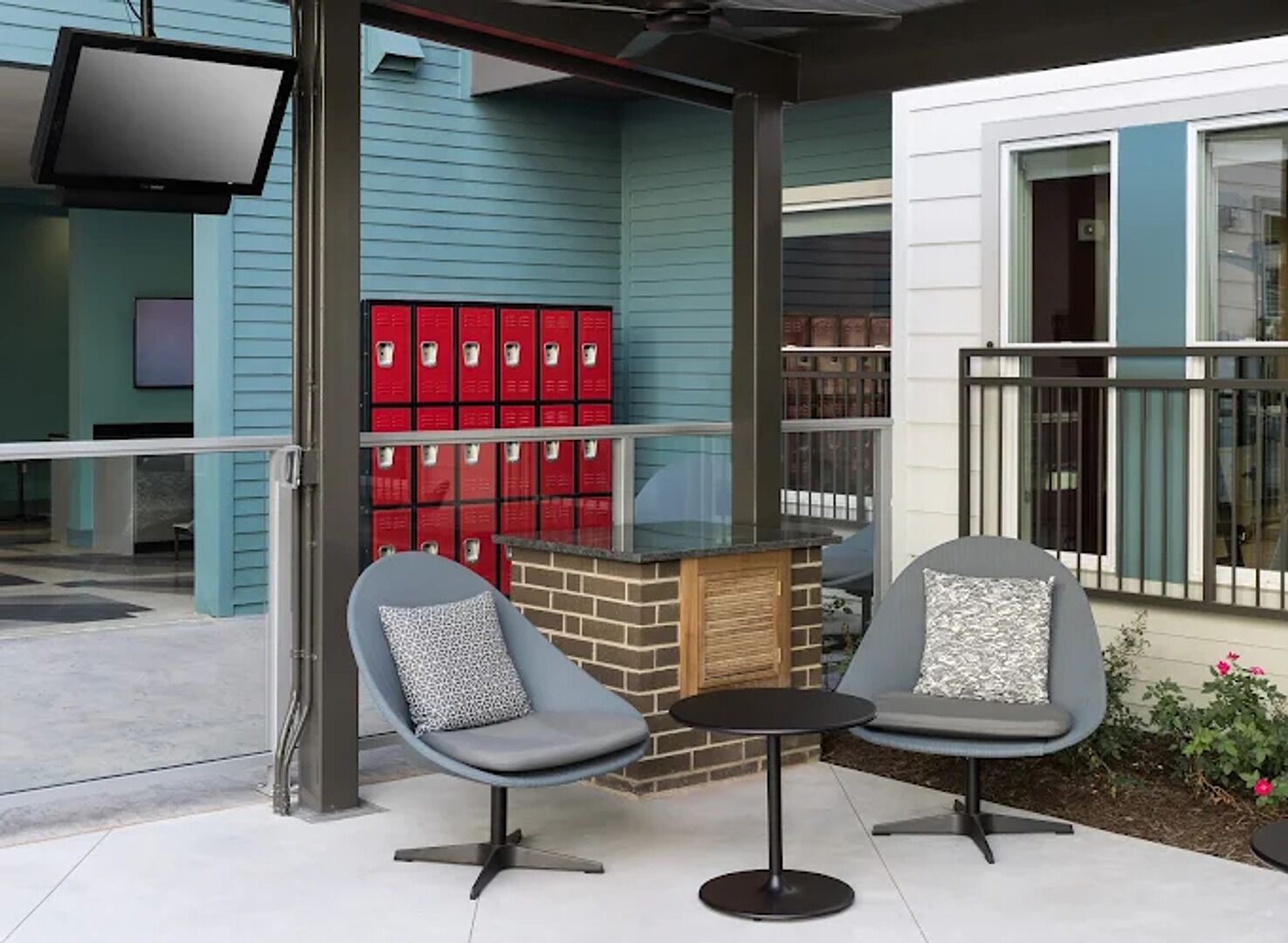 Een zithoek met twee stoelen en een kleine tafel, een rode brievenbus, en een gebouw met blauwe bekleding en een balkon.