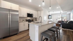 Una cocina moderna con electrodomésticos de acero inoxidable, una isla central con taburetes y un comedor con sofá y sillas.