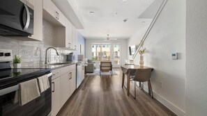 A modern kitchen with a microwave, stove, and sink, leading to a dining area with a table and chairs. - Landing | Amazing 1BD, Clubhouse (Austin)