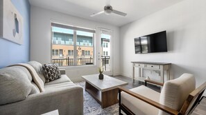 A modern living room with a sofa, armchair, coffee table, and a flat-screen TV mounted on the wall. - Landing | Amazing 1BD, Clubhouse (Austin)