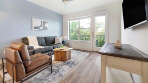 A living room with a sofa, a leather chair, a coffee table, and a TV mounted on the wall. - Landing | Amazing 1BD, Clubhouse (Austin)