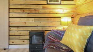 Una habitación acogedora con paredes de madera, una pequeña estufa negra, una manta colorida y una almohada amarilla.