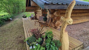 Una cabaña de troncos con terraza de madera, asientos exteriores y una gran escultura de madera.
