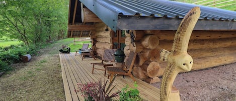 Une cabane en rondins dotée d’une terrasse en bois, de meubles d’extérieur et d’une grande sculpture en bois.