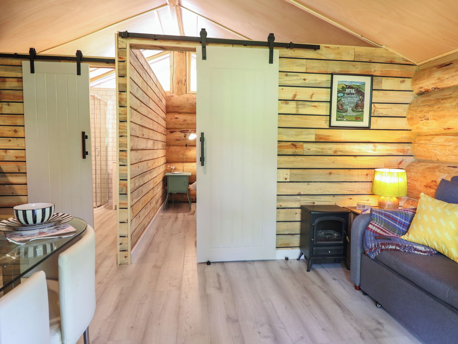 Interior acogedor de una cabaña de troncos con comedor, sofá, lámpara y chimenea.