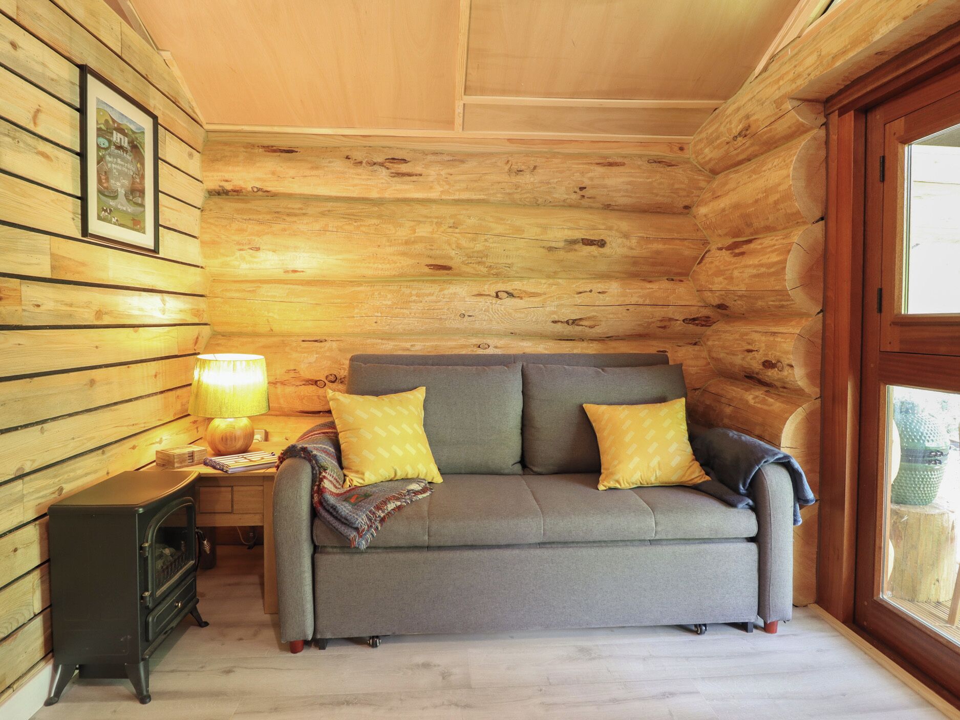 Una acogedora habitación de cabaña de madera con sofá, una mesa con lámpara y un cuadro enmarcado en la pared.