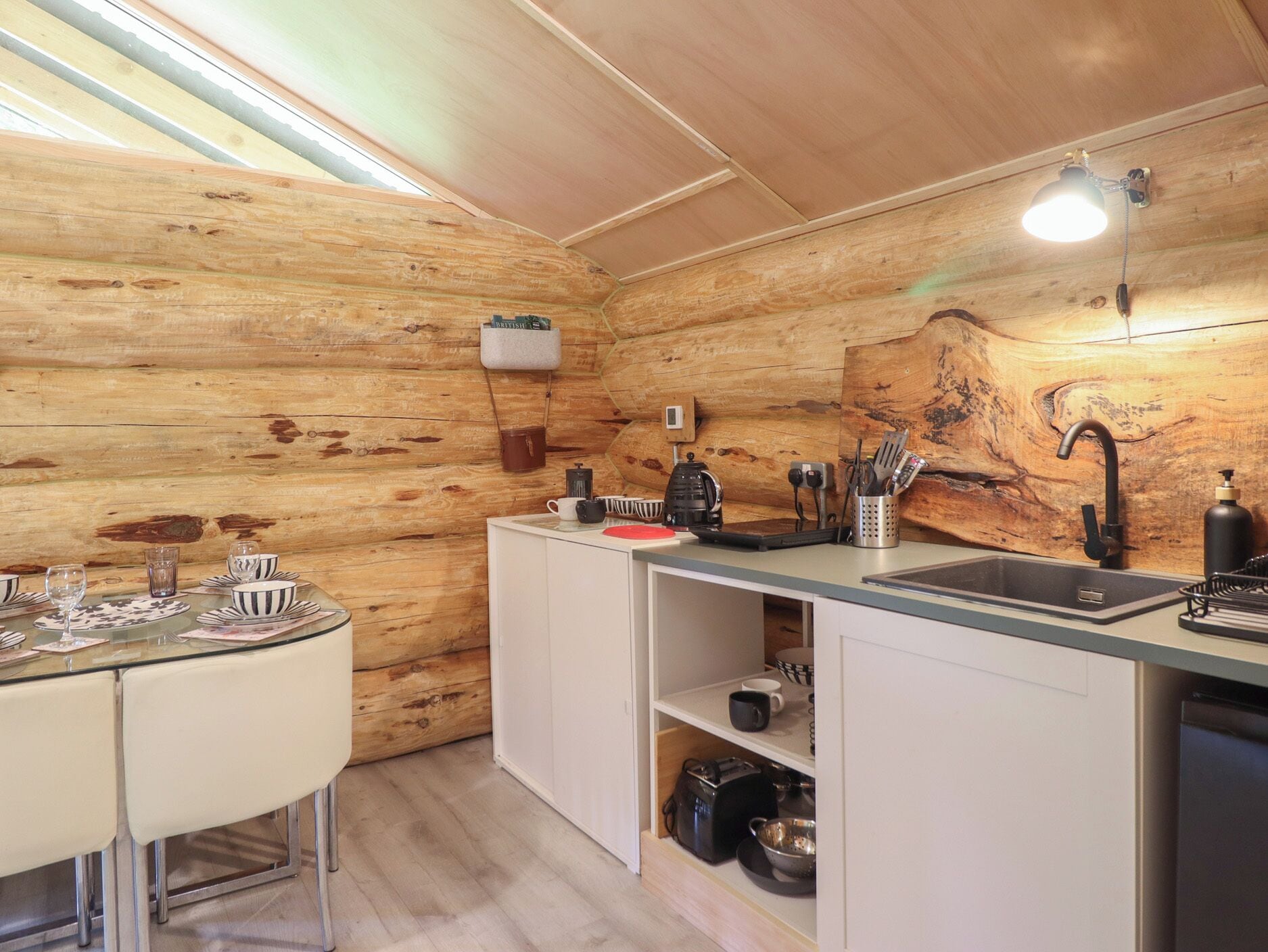 Cocina compacta con paredes de madera, una mesa de comedor con sillas, un fregadero y una encimera con diversos utensilios de cocina.