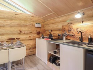 Une cuisine compacte aux murs en bois, avec une table à manger et des chaises, un évier et un plan de travail sur lequel sont disposés divers ustensiles de cuisine.