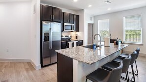 A modern kitchen with a central island, stainless steel appliances, and a view of the outdoors. - Landing | Beautiful 2BD, Pool, Gym (Austin)