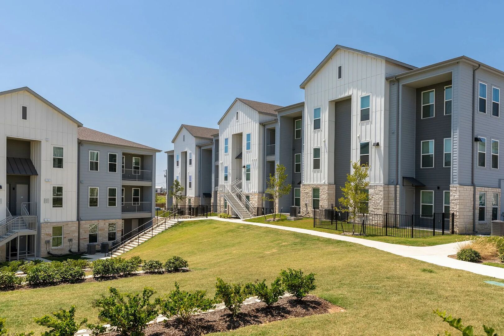 A modern apartment complex with multiple-story buildings, a central courtyard, and a well-maintained lawn.