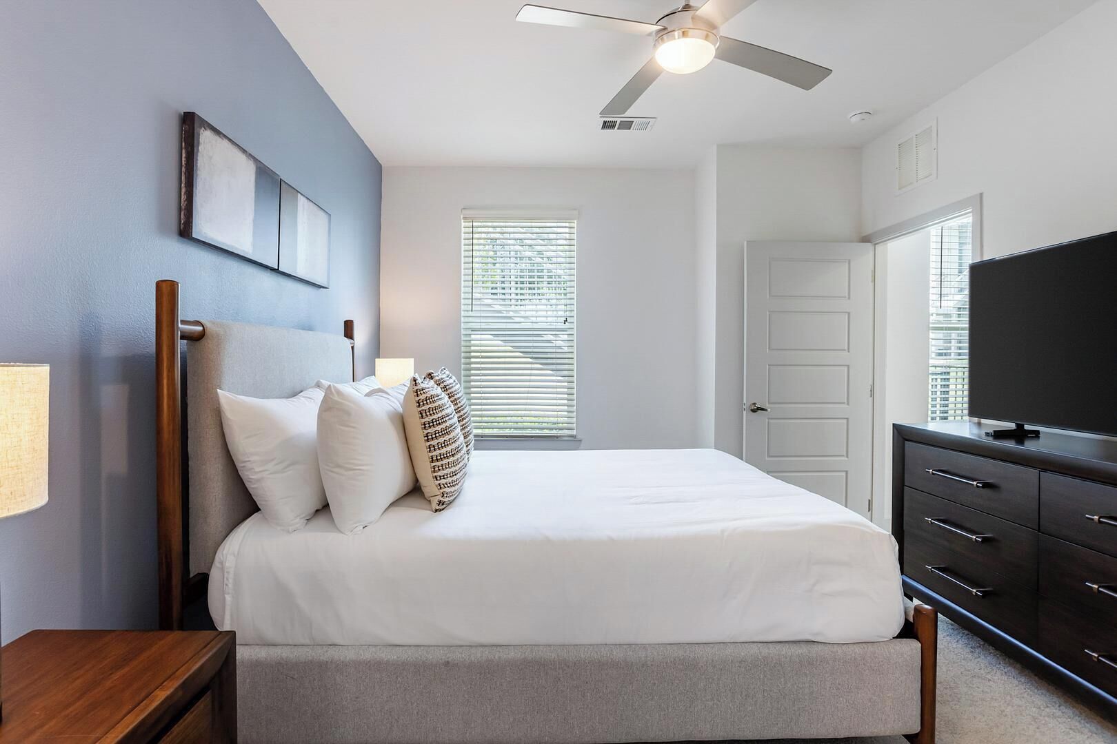 A bedroom with a bed, a ceiling fan, a dresser, and a television.