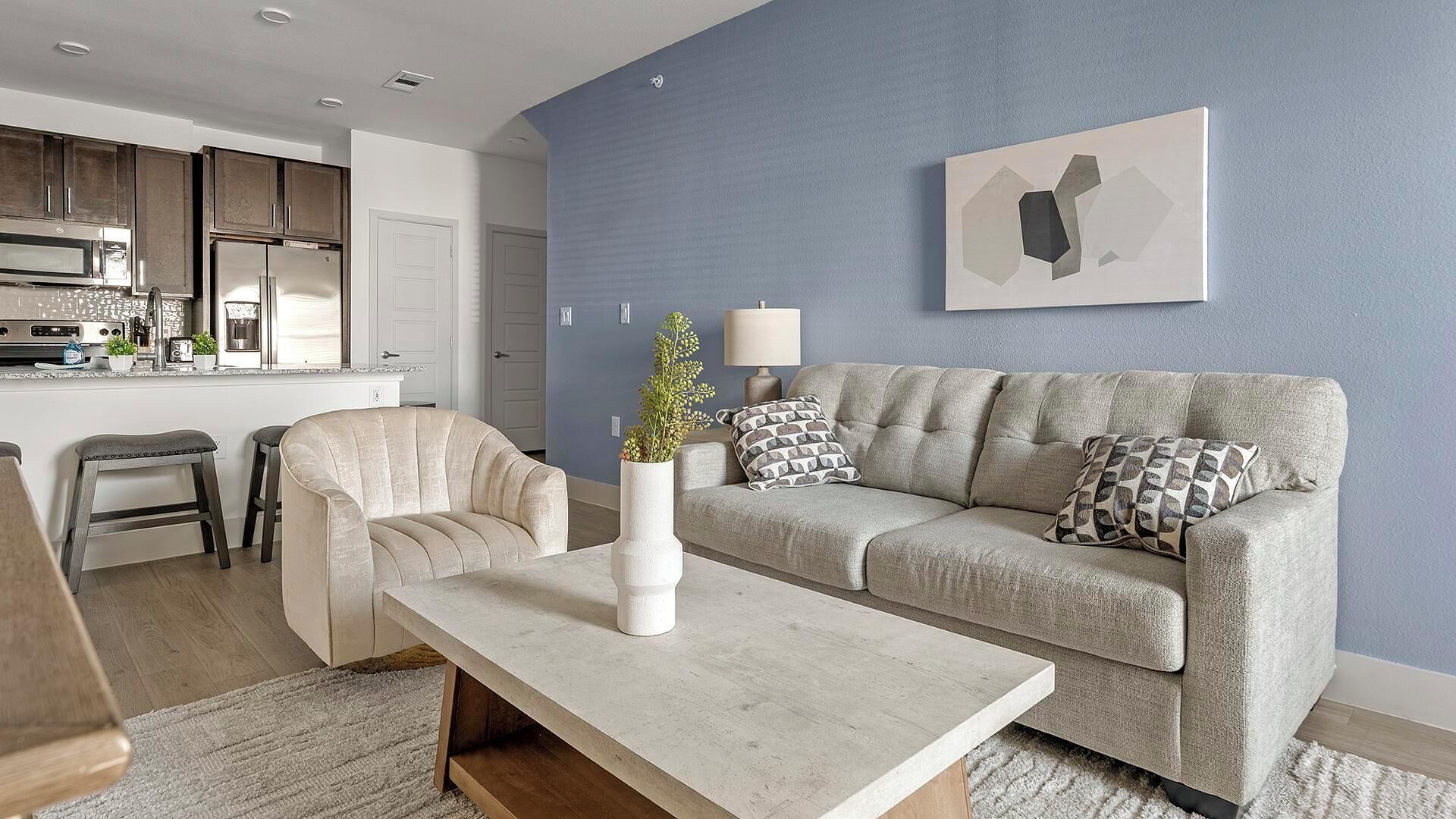A modern living room with a sofa, armchairs, a coffee table, and a kitchen in the background.