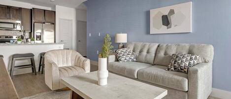 A modern living room with a sofa, armchairs, a coffee table, and a kitchen in the background.