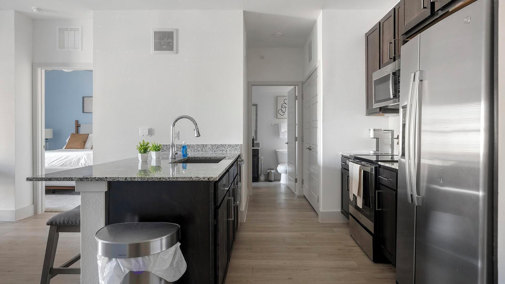 A modern kitchen with a central island, stainless steel appliances, and a view into a bedroom.