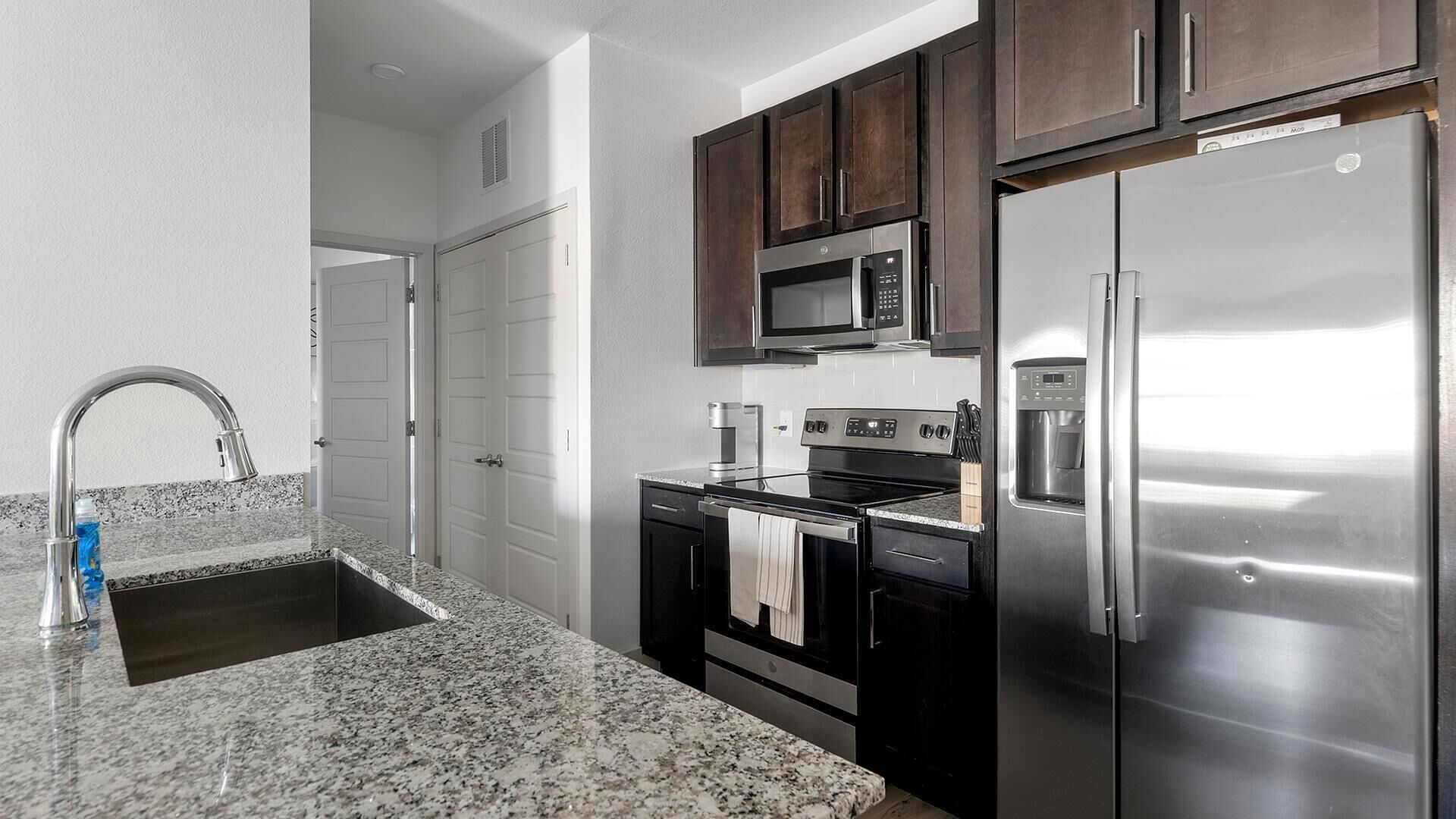 A kitchen with granite countertops, stainless steel appliances, and dark wooden cabinets.