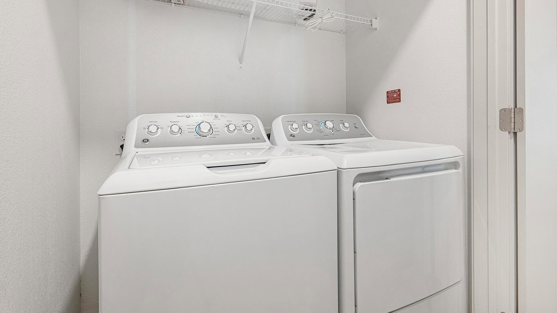 A laundry room with two white washers and dryers, a clothes drying rack, and a fire safety sign on the wall.