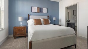 A bedroom with a bed, nightstands, a dresser, and a bathroom visible through an open door. - Landing | Spectacular 2BD, Pool, Gym (Austin)