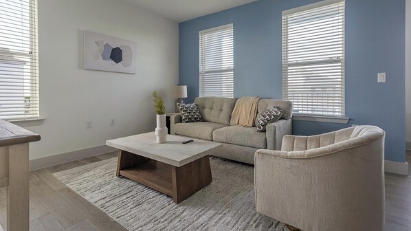 A living room with a sofa, armchair, coffee table, and a painting on the wall. - Landing | Spectacular 2BD, Pool, Gym (Austin)