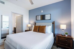 A hotel room with a large bed, two bedside tables with lamps, a small potted plant, and a door leading to another room. - Landing | Stylish 1BD, Gym, Pool (Austin)