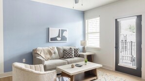 A living room with a sofa, a coffee table, a lamp, and a window with blinds. - Landing | Stylish 1BD, Gym, Clubhouse (Asheville)