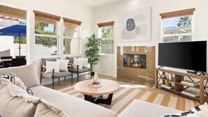Ein modernes Wohnzimmer mit einer Couch, einem Couchtisch, einem Fernseher, einem Kamin und großen Fenstern.