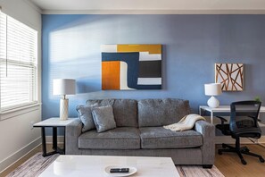 Un salon avec un canapé gris, une table basse, un téléviseur et un bureau avec une chaise.