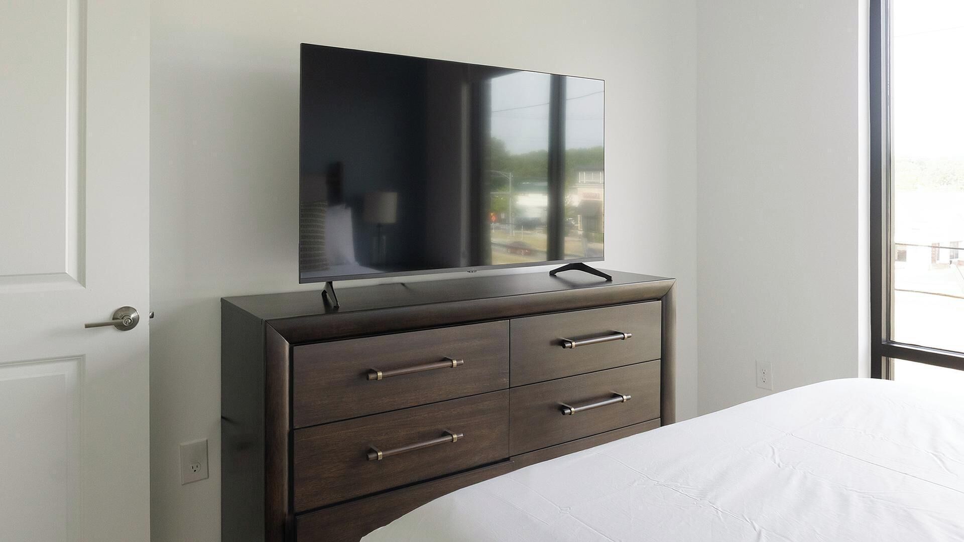 Een slaapkamer met een bed, een dressoir met lades, een flatscreen-tv aan de muur en een raam met uitzicht.