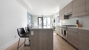 Eine moderne Küche mit einer zentralen Kochinsel, Barhocker, einem Einbauofen und einem großen Fenster.