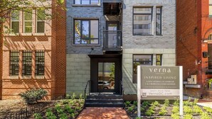 Un bâtiment moderne avec une façade en briques, une entrée en verre et une enseigne publicitaire pour des appartements de luxe.