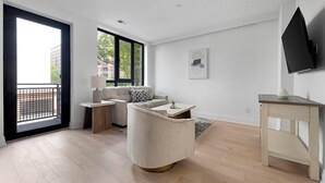 A modern living room with a sofa, coffee table, and a TV mounted on the wall. - Landing | Incredible 2BD in Logan Circle (Washington)