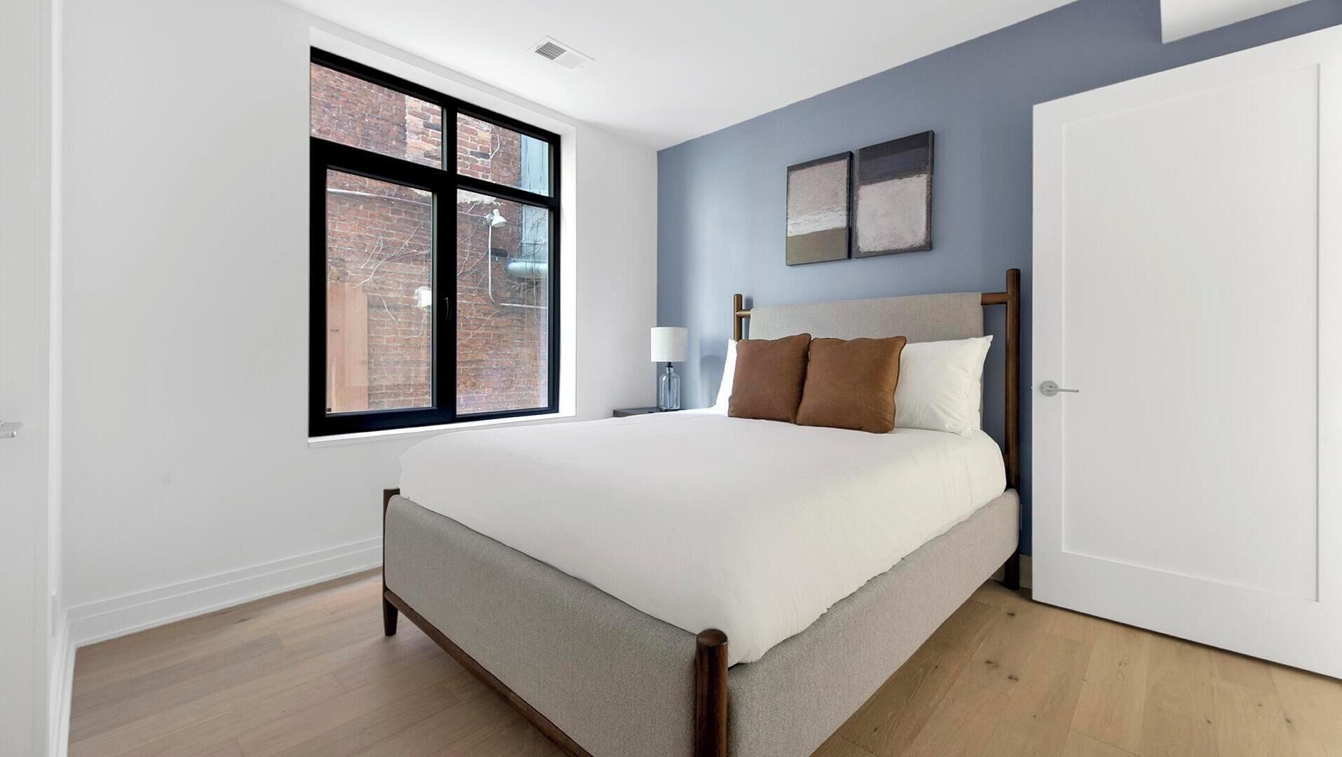 Een slaapkamer met een bed, een raam, een nachtkastje, een lamp en een deur.