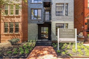 A modern building with a brick facade, a glass entrance, and a signboard advertising luxury condominiums. - Landing | Chic 2BD in Logan Circle (Washington)