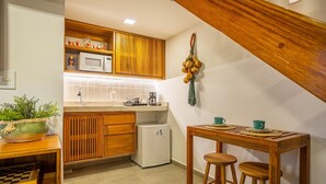 A kitchen with wooden cabinets, a white refrigerator, a wooden dining table with stools, and a hanging decorative item. - Arara House 1 (Jijoca de Jericoacoara)