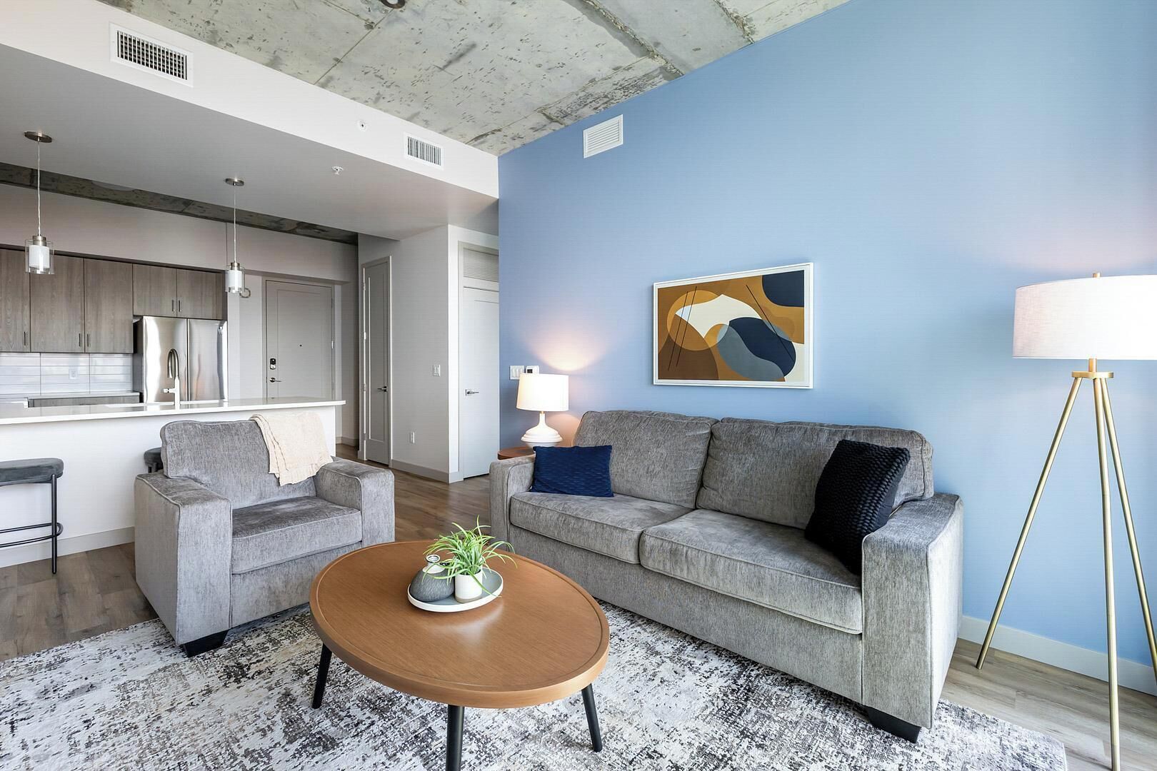 A modern living room with a grey sofa, a coffee table with a plant, a lamp, and a painting on the wall.