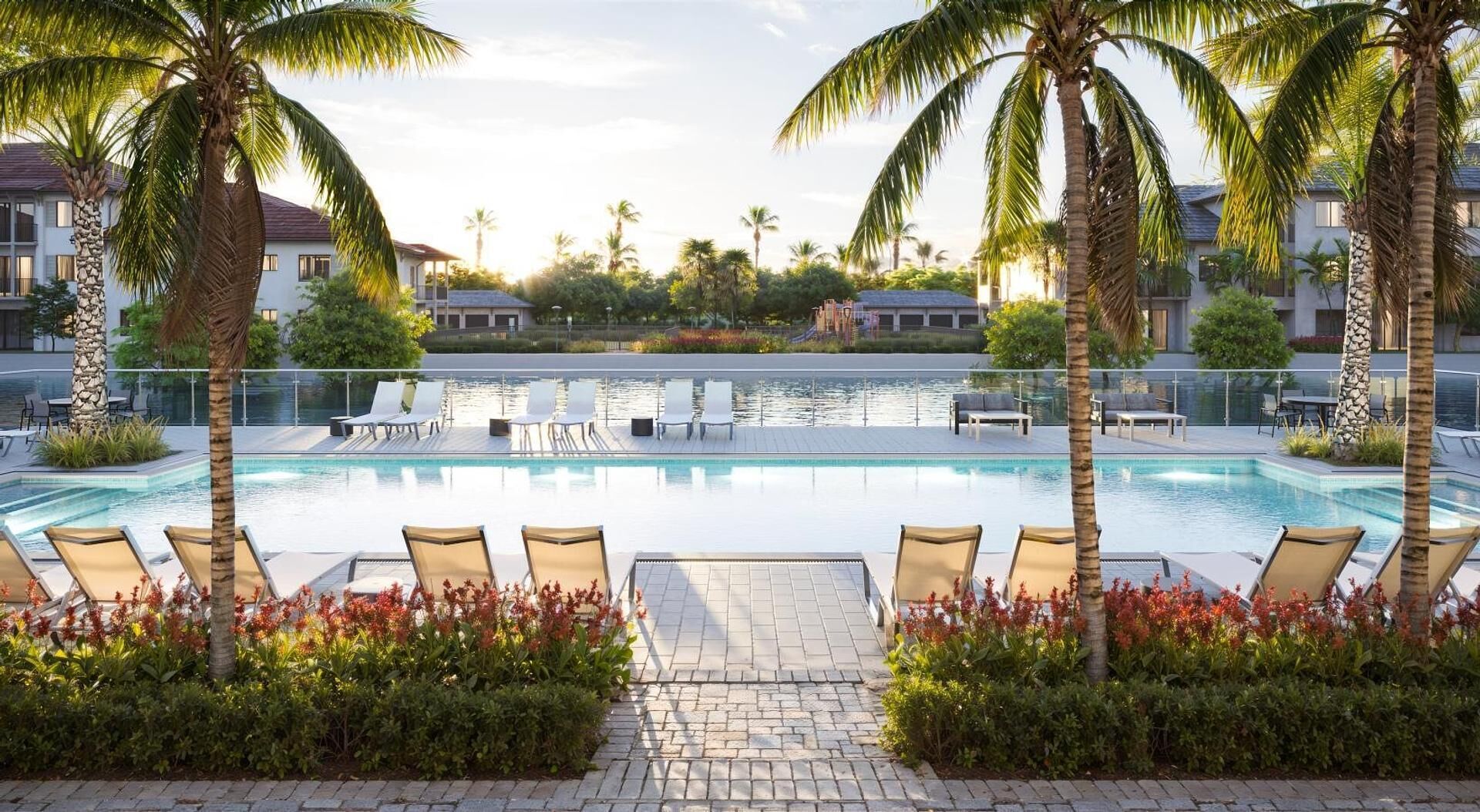 A swimming pool with lounge chairs, palm trees, and a view of buildings in the background.