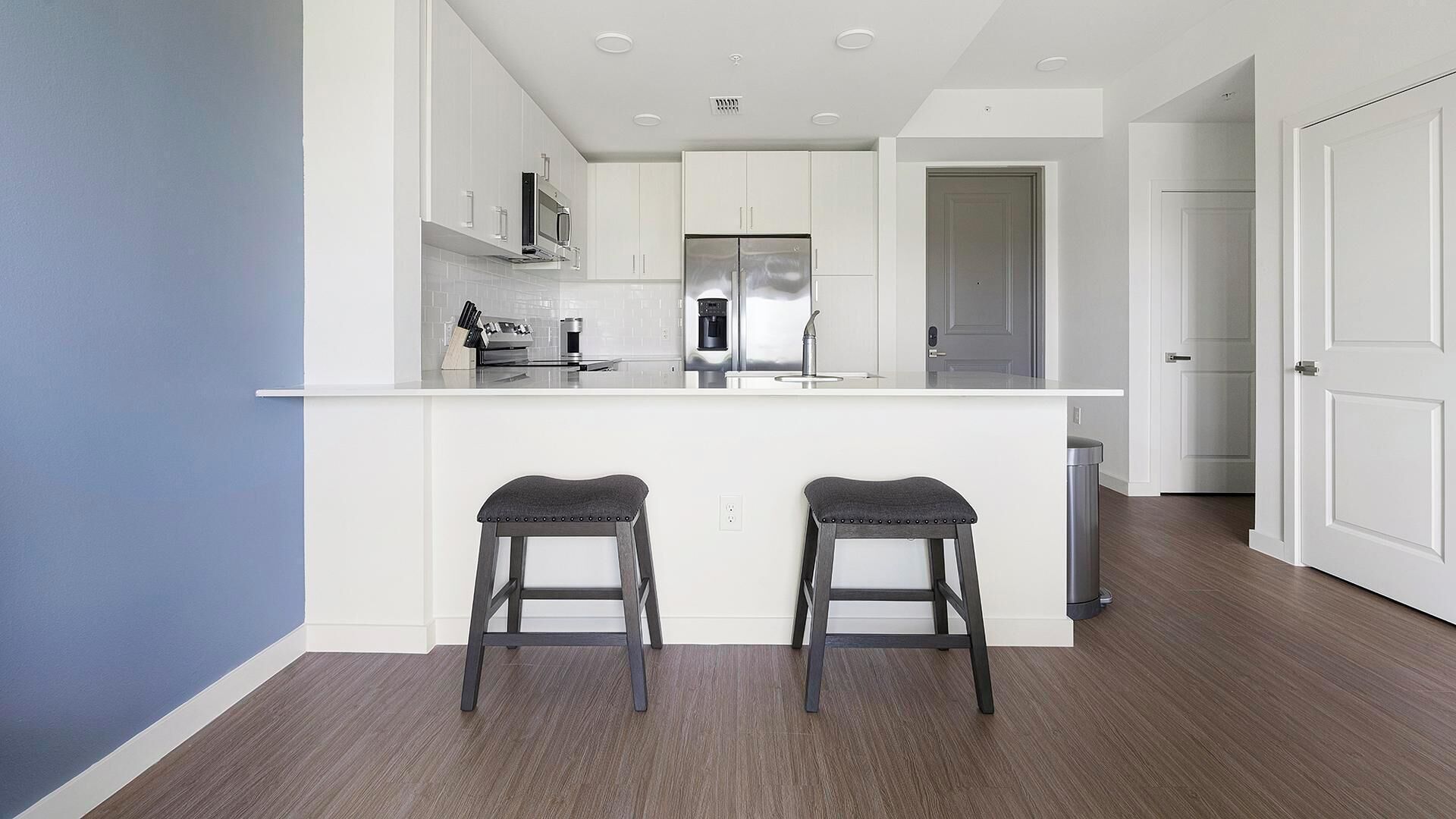 Una cocina moderna con armarios blancos, electrodomésticos de acero inoxidable y una zona con taburetes de bar.