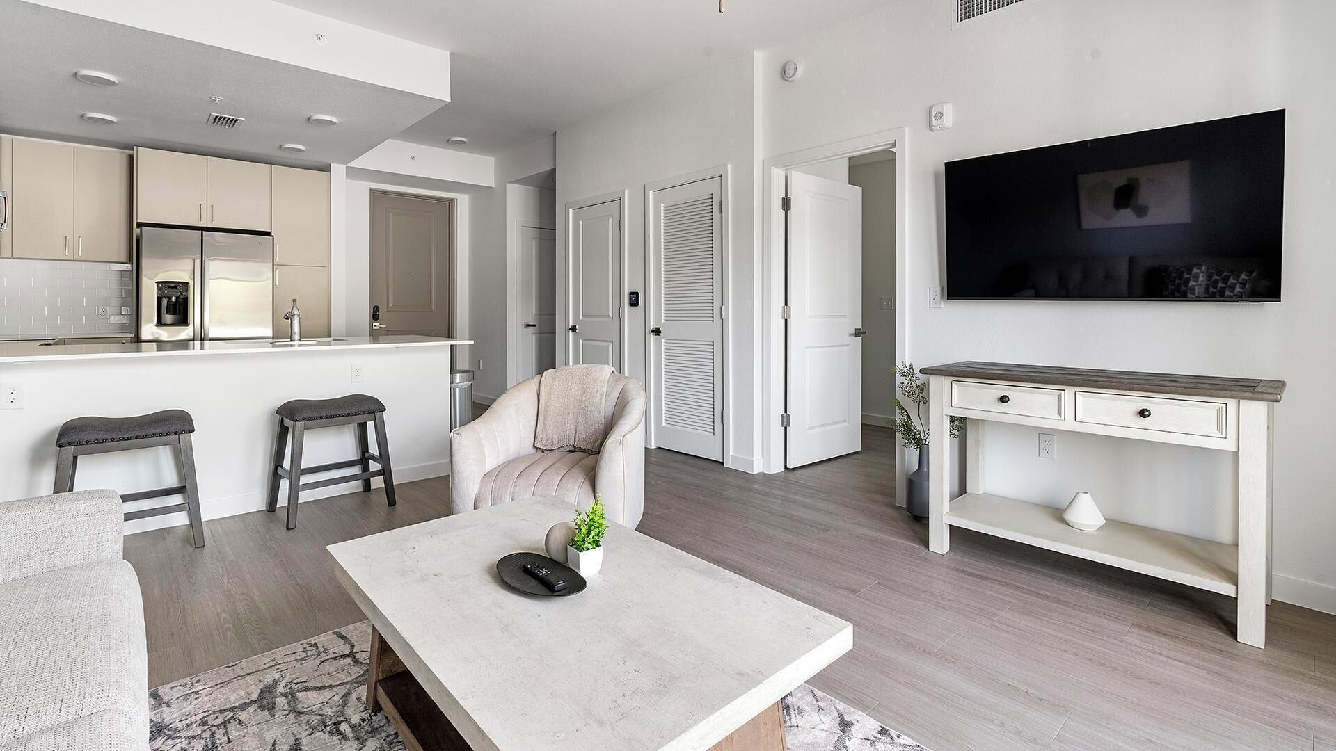 Una sala de estar moderna con un sofá, una mesa de centro, un televisor y una cocina con armarios y un refrigerador.