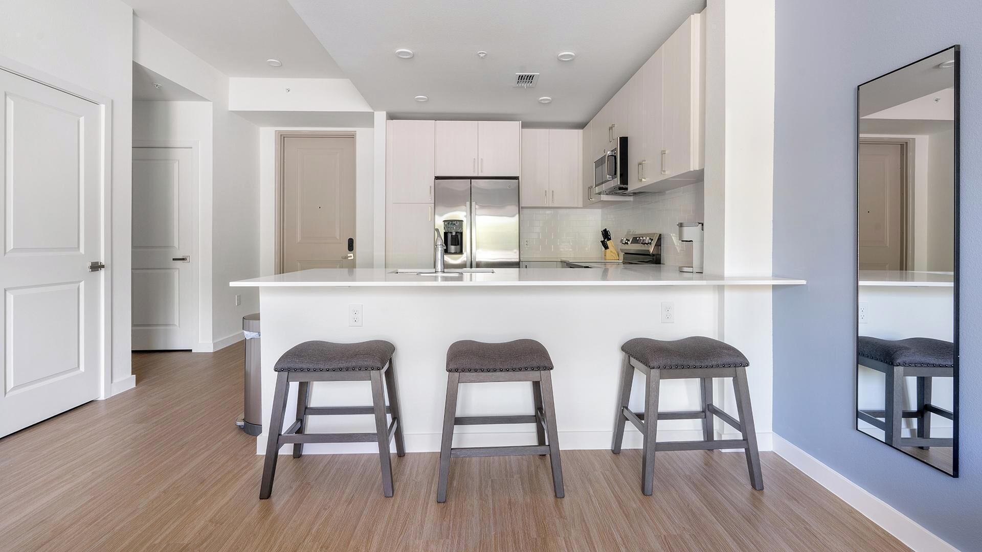 Een moderne keuken met een centraal eiland, drie krukken en een grote spiegel.