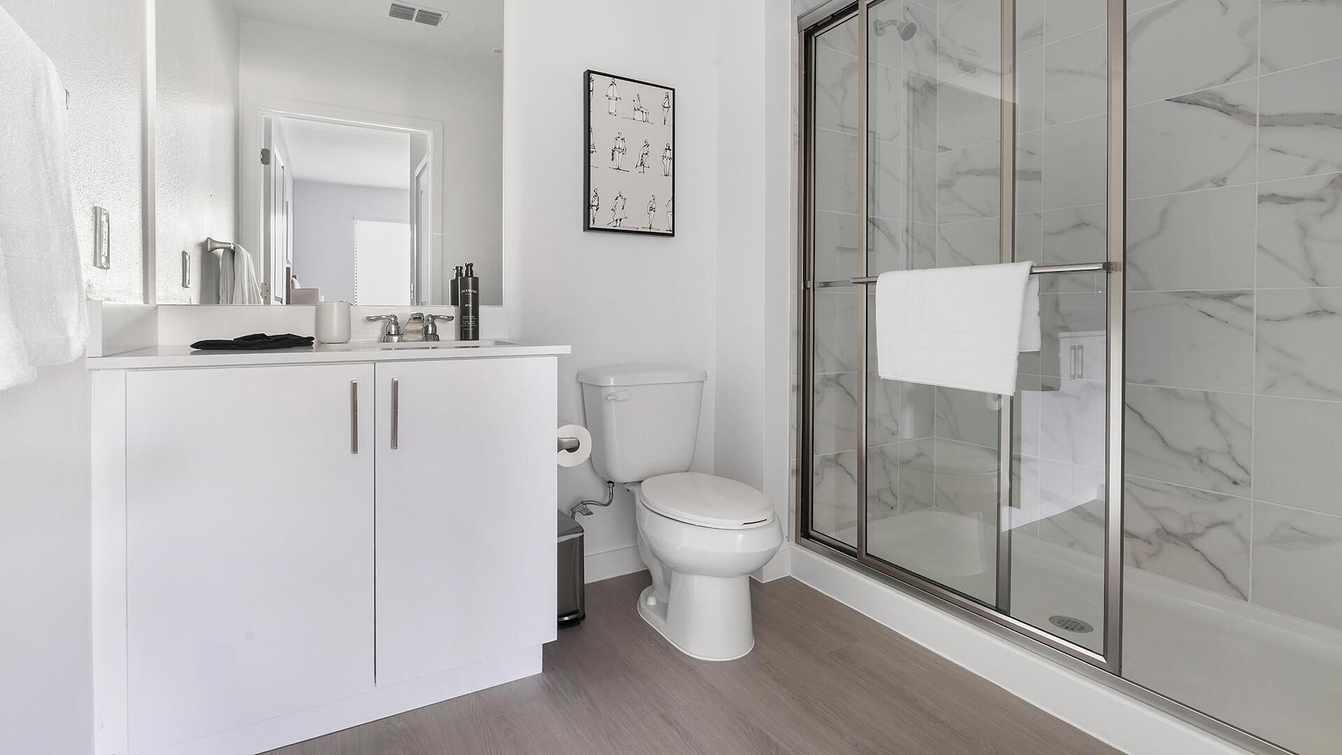 A modern bathroom with a white vanity, a toilet, a glass shower enclosure, and a marble backsplash.