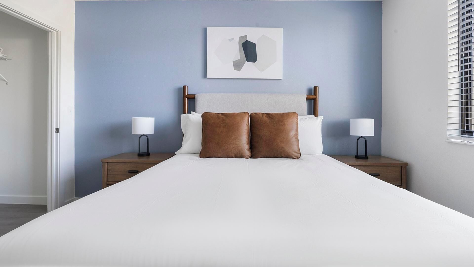 A bed with two nightstands, a headboard, and a wall-mounted abstract art piece.