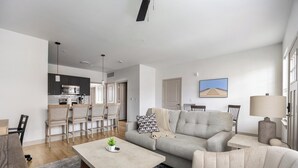 Ein modernes Wohnzimmer mit einer Couch, Sesseln, einem Couchtisch sowie einem Essbereich mit Stühlen und einer Küche im Hintergrund.